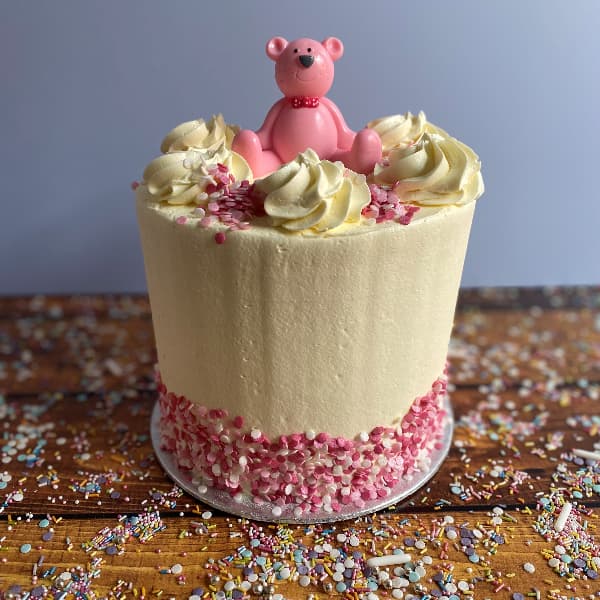 Tall Teddy Bear Pin Buttercream 2023 Tall Buttercream Cake with a Pink teddy Topper and Pink Sprinkles around the bottom of the cake